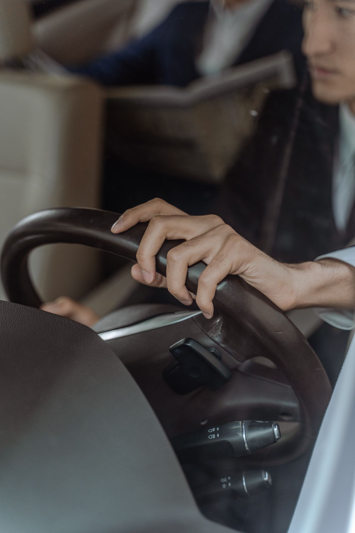 Close-up of a chauffeur's hands on the steering wheel with a passenger reading in the back seat