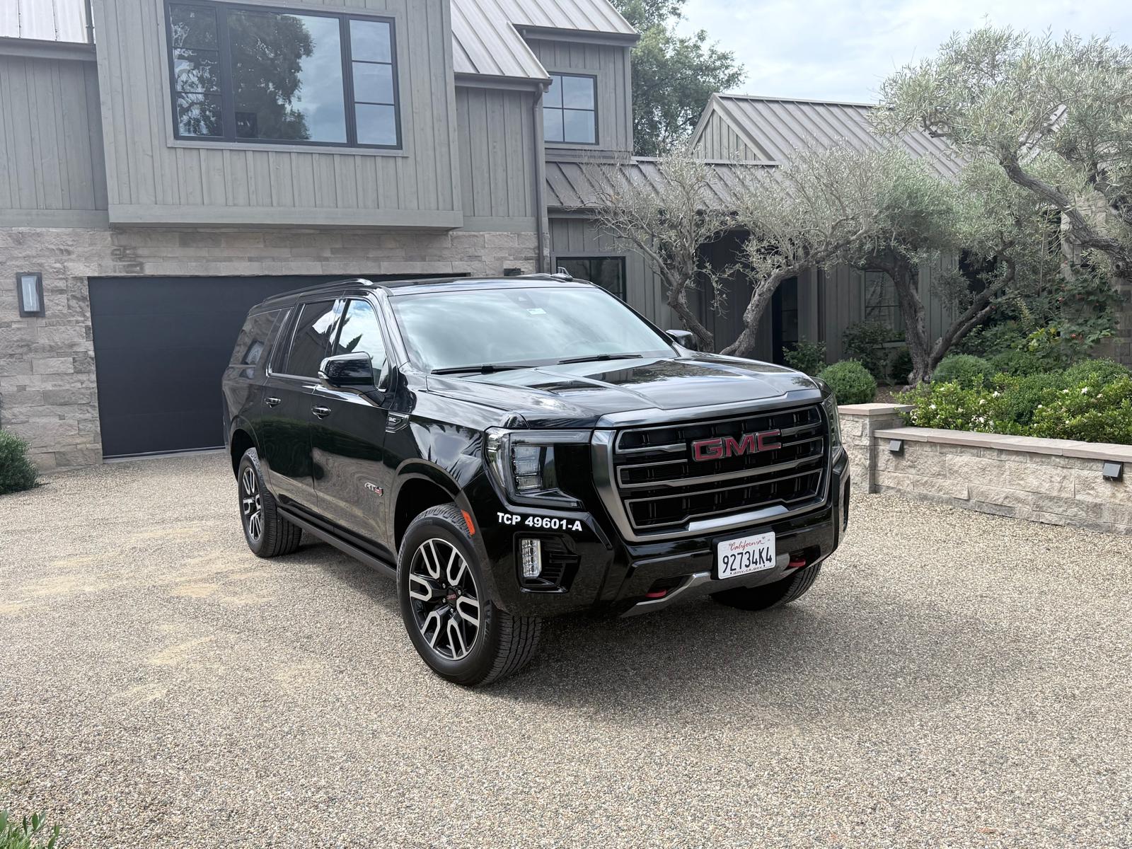 Jet Car Limo's black GMC Yukon XL AT4 marked TCP 49601-A on a gravel driveway in front of a modern estate