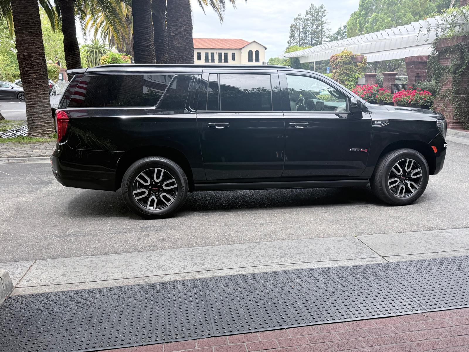 Side profile of Jet Car Limo's black GMC Yukon XL AT4 waiting at a hotel entrance lined with palm trees