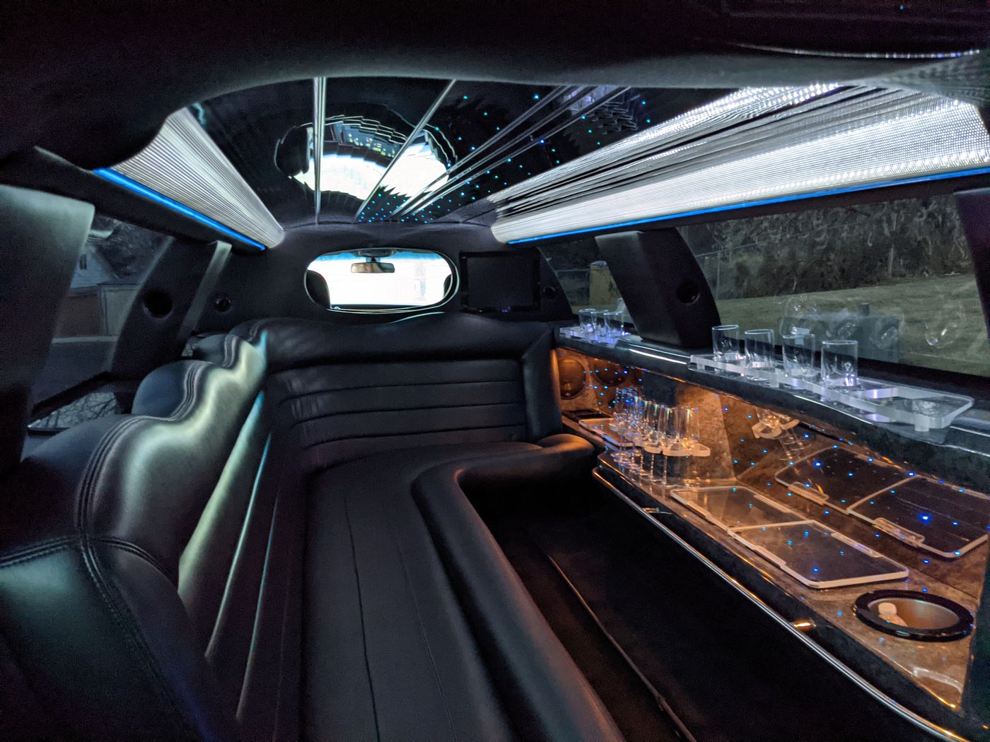 Inside a stretch limousine: black leather bench seating, a lit bar with glassware and a fiber-optic starlight ceiling