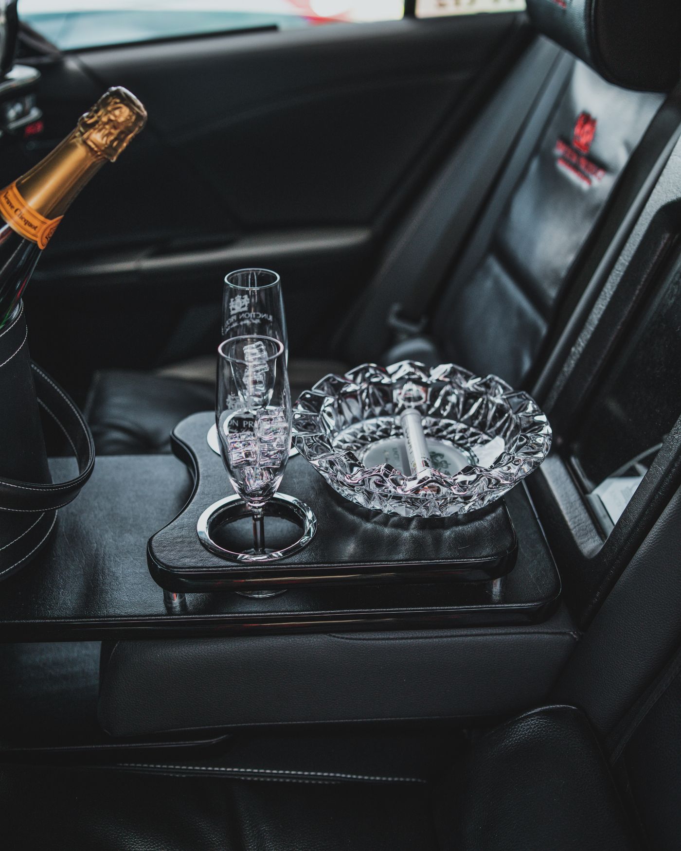 A chilled champagne bottle, crystal flutes and a cut-glass ashtray on the rear console of a limousine
