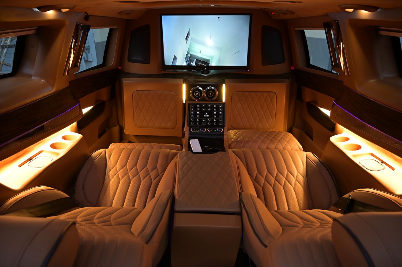 Interior of an executive van with quilted tan leather captain's chairs, ambient lighting and a rear screen