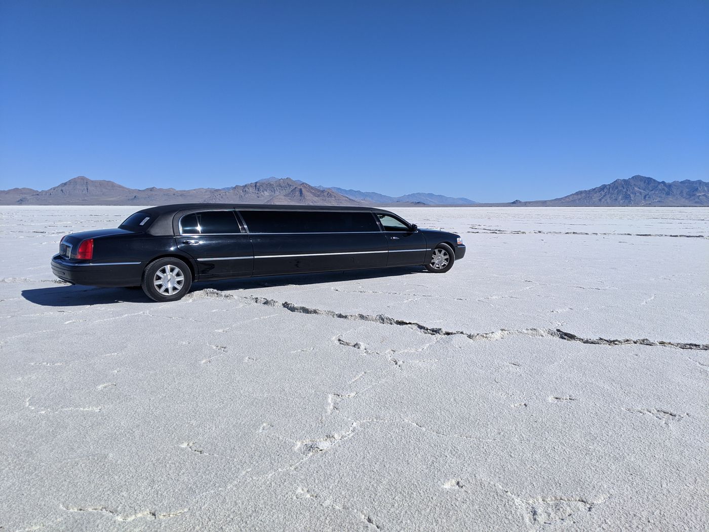 A black stretch limousine parked on a wide open salt flat under a clear blue sky